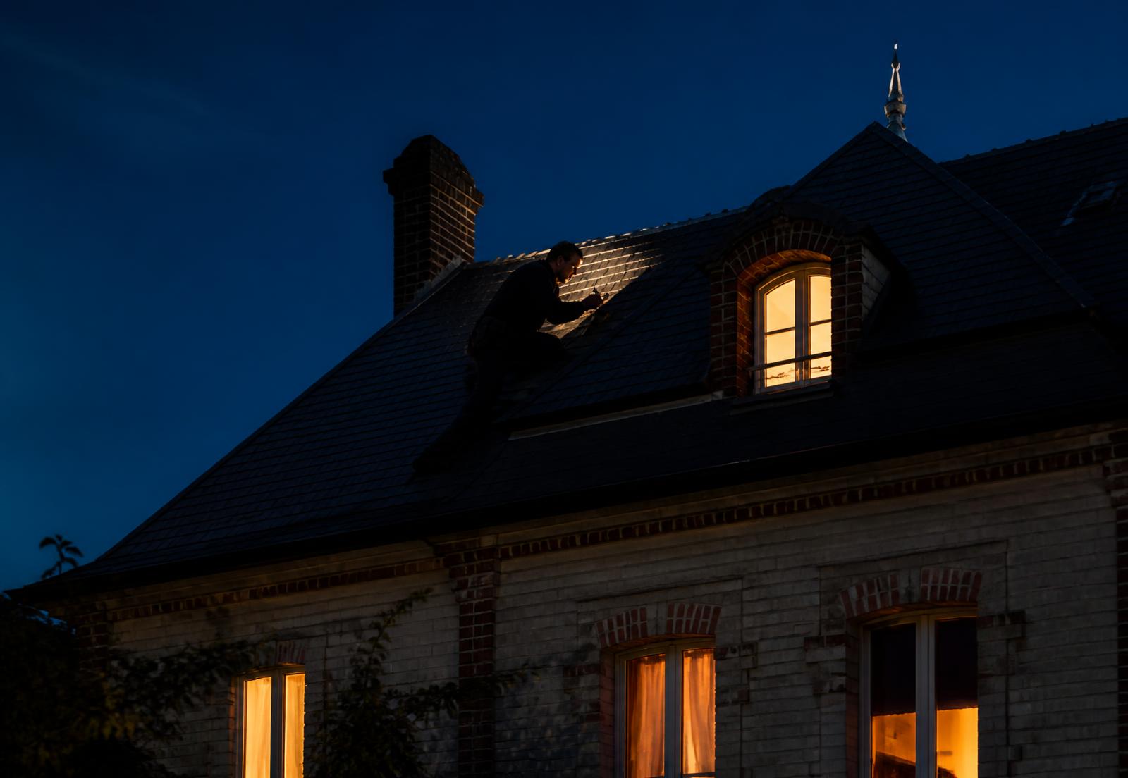 Couvreur au travail sur un toit en ardoise d'une maison rémoise à la tombée de la nuit